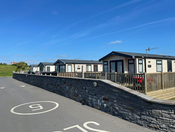 Grey Brick Wall and a road showing the entrance to shoreline caravan park. There are four white caravans in the background.