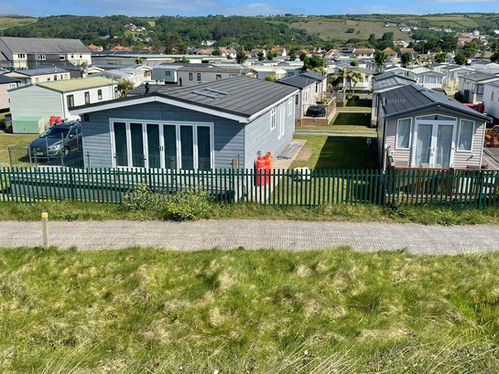 A grass area and coastal path with many caravans in the background.
