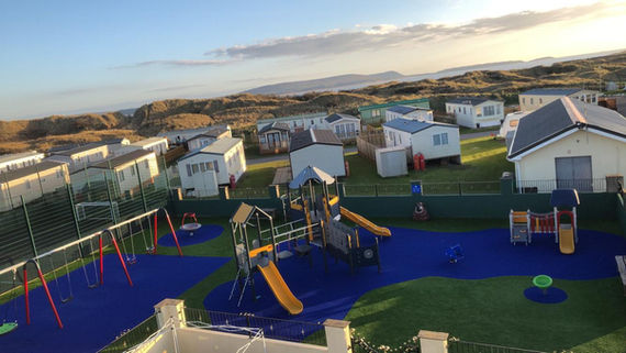 Top down view of a children's outdoor play park. There are yellow slides, red swings, and a football court.