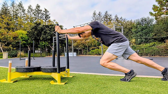 A male athlete performs a heavy sled push on artificial turf as part of an athletic performance and strength training workout