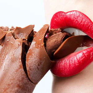 Red lips biting a cracked chocolate ice cream bar with frosty surface. Close-up, white background, highlighting glossy lipstick and texture.
