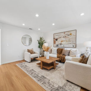 A bright, modern living room with a white sofa, abstract wall art, a round mirror, and light oak floors.