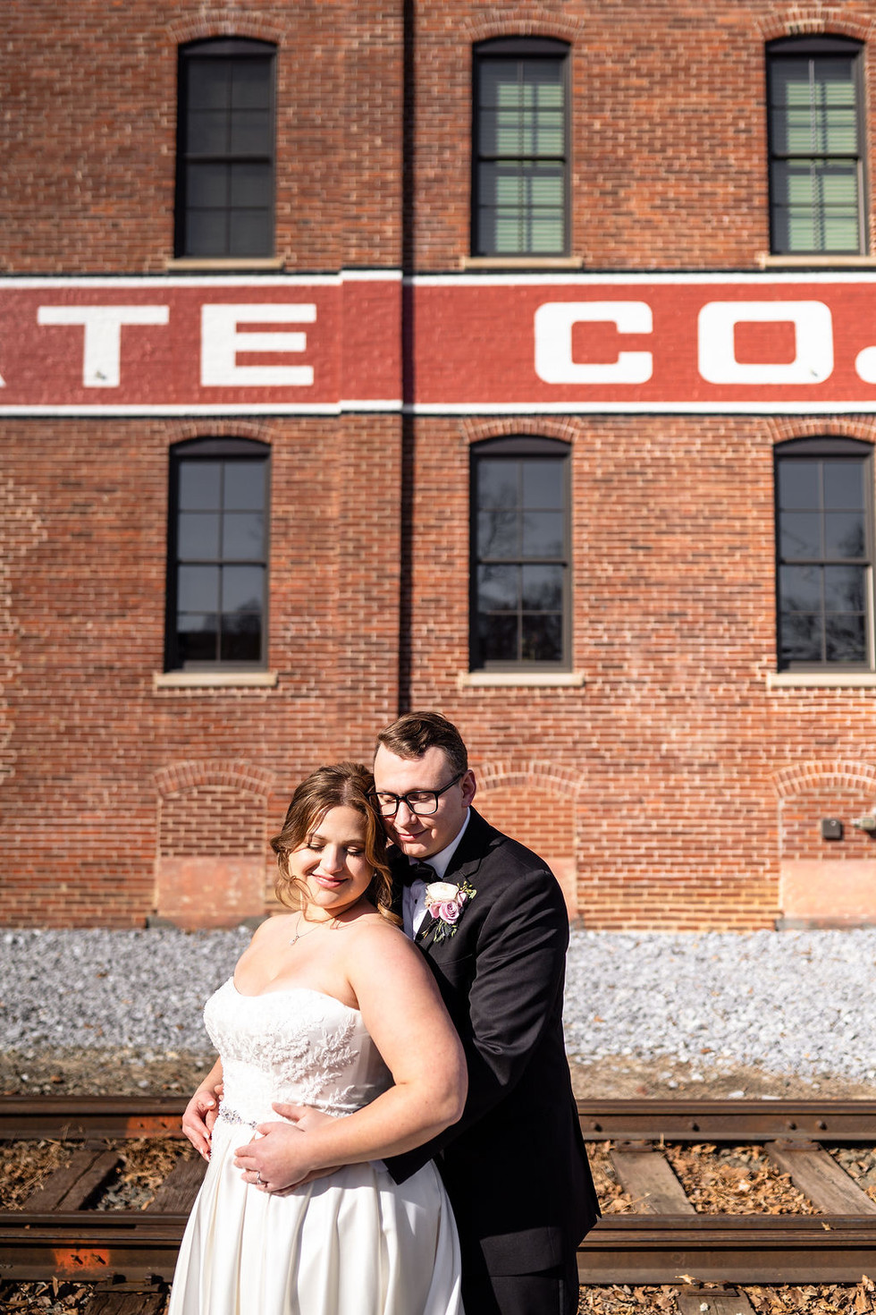 bride and groom posing in the sun in front of a brick building Lititz Spring Park in Lititz Pennsylvania