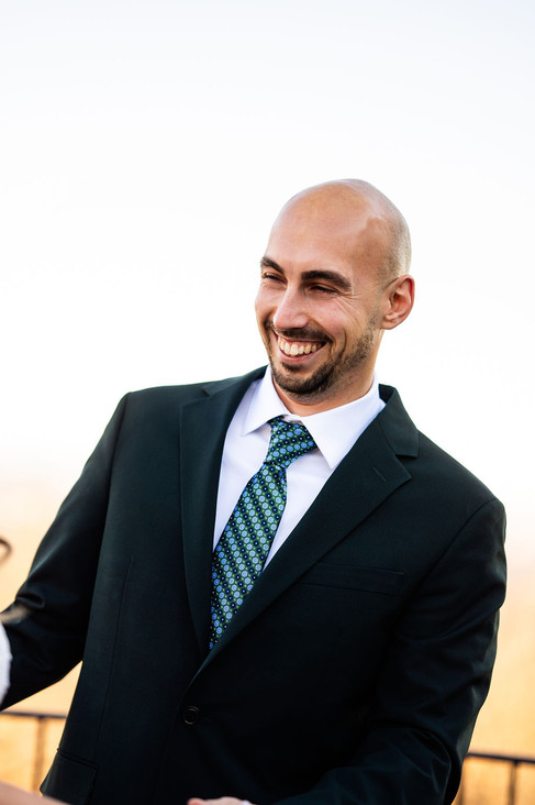a groom in a suit smiling at his bride