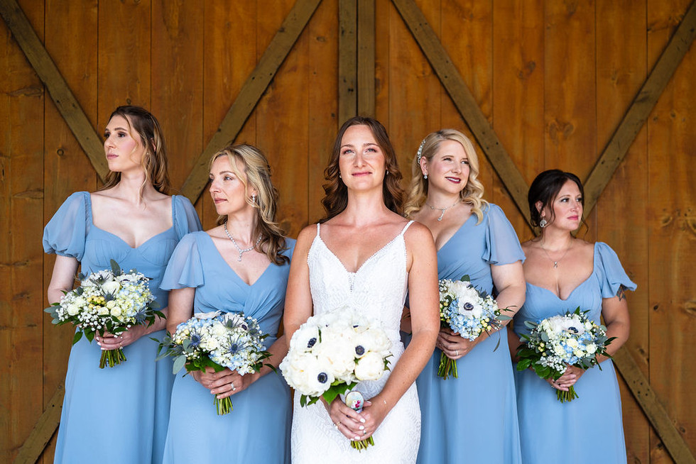a bride in a white bridal gown with bridesmaids in light blue dresses looking away from the camera in front of a barn door at Reinhart's Barn on Oak Lane in Bernville, Pennsylvania