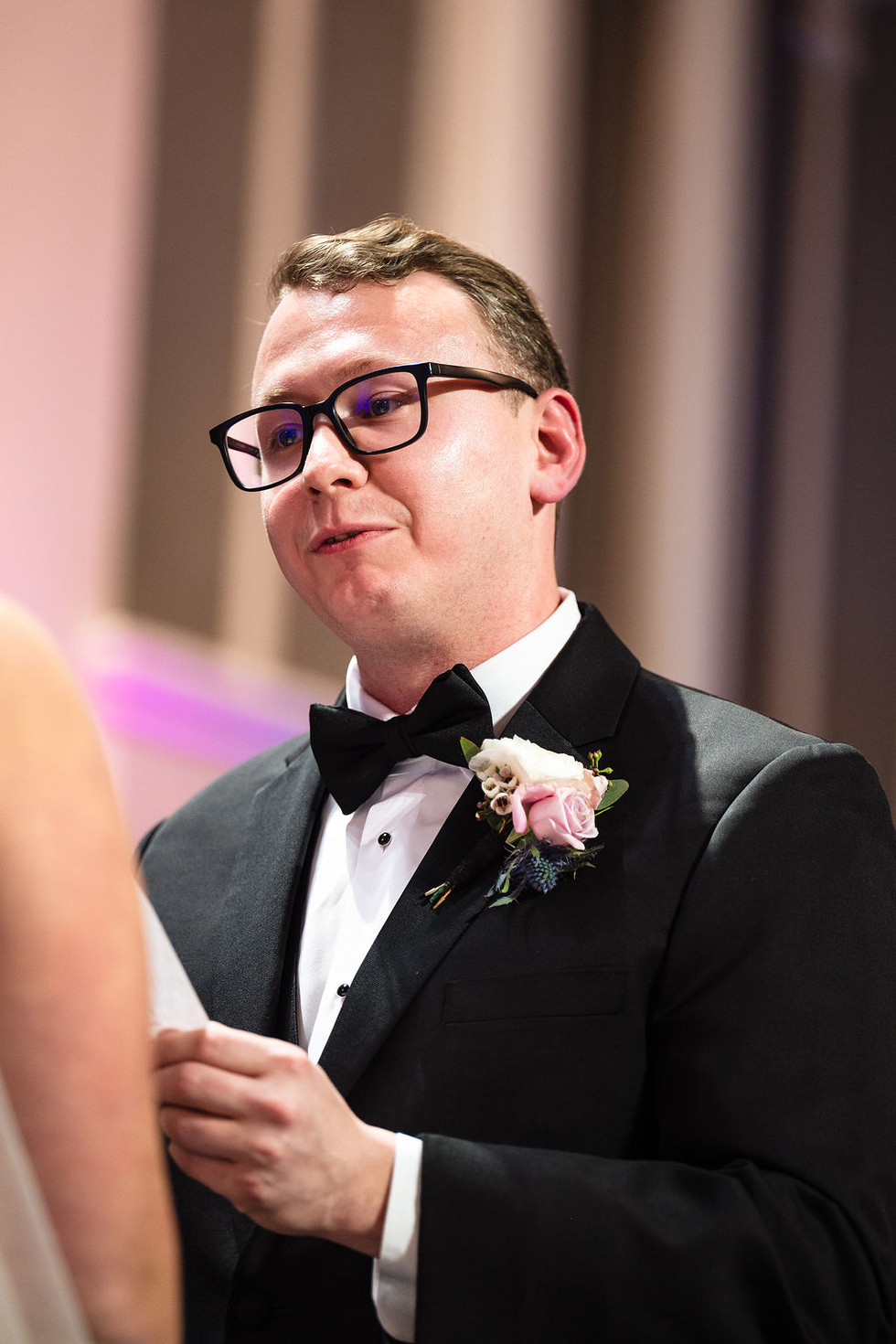 a man in a black suit black bowtie and pink flowers