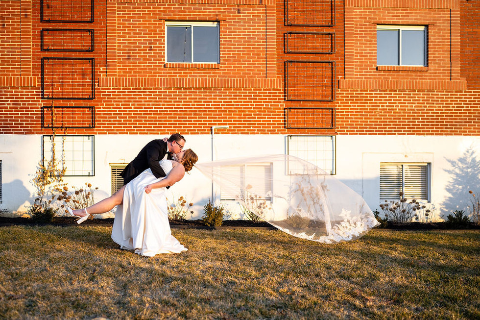 a groom dipping his bride with a white veil blowing in the wind in front of Lincoln Shoe Co. in Lititz Pennsylvania