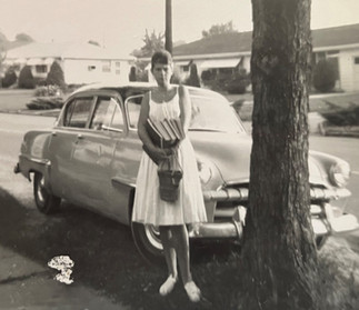 girl with school books standing in front of 1940s model automobile