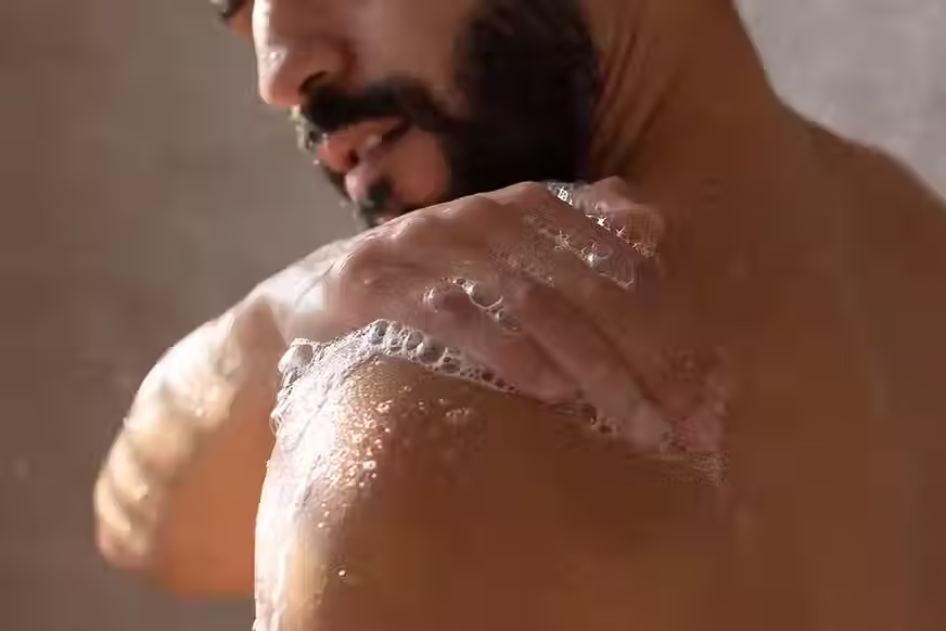 Persona lavándose el hombro con un jabón suave, creando una abundante espuma que cubre la