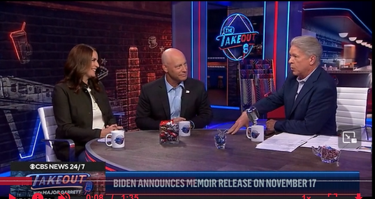 A journalist interviews a man and a woman in a news studio.