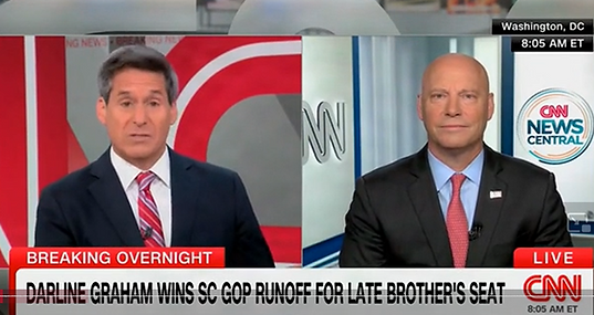 Two men in suits with a split screen, both in separate news studios. At the bottom of the screen, a breaking news bulletin saying, "Darline Graham Wins SC GOP Runoff for Late Brother's Seat."
