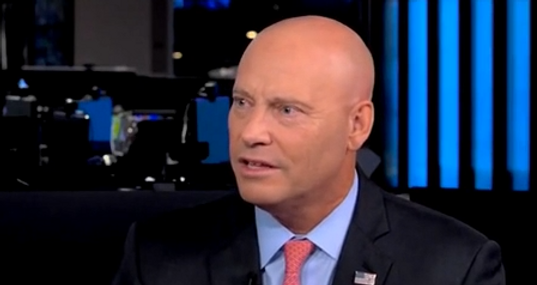A man in a suit in a news studio speaks.