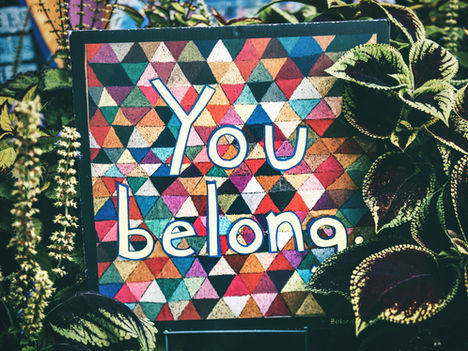 Outdoor welcome sign for a store that reads "You belong" and has multi-colored triangle pattern background.