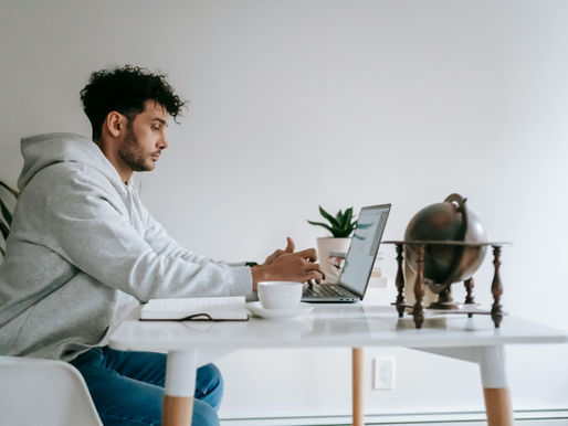 Virtual Assistant working on laptop at home office table with coffee and globe decor.