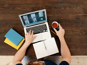A client having a virtual meeting on a laptop with his team, with coffee and notebooks on a wooden table.
