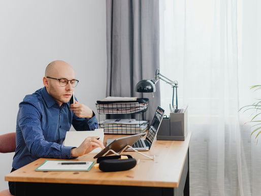 A Business Man Sitting at a Desk Looking at a Tablet While Holding a Phone
