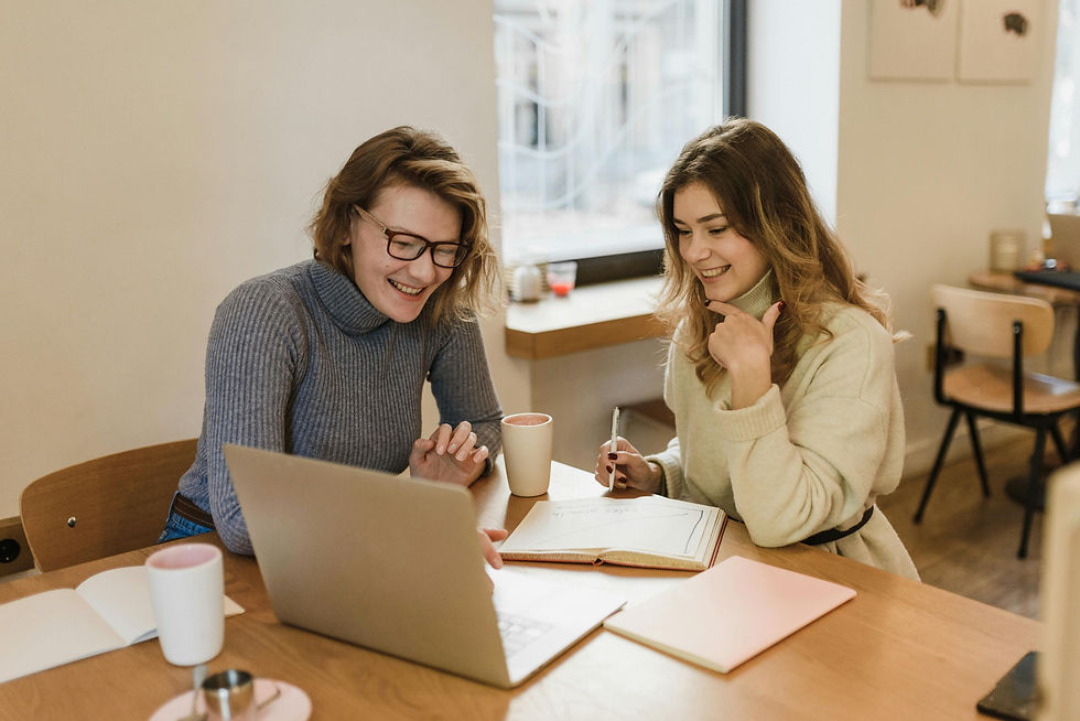 Two Virtual Assistants laughing and working together in a cozy office setting with laptops and notebooks.