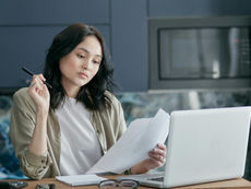 A Virtual Assistant reviewing documents and working on a laptop in a modern home office setting.