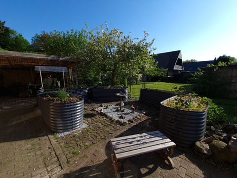 Sonniger Garten mit Hochbeeten und Bank