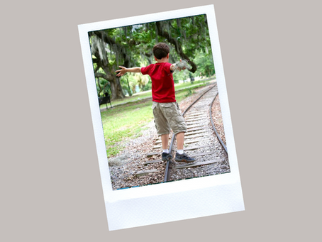 Little boy walking on train tracks in a park