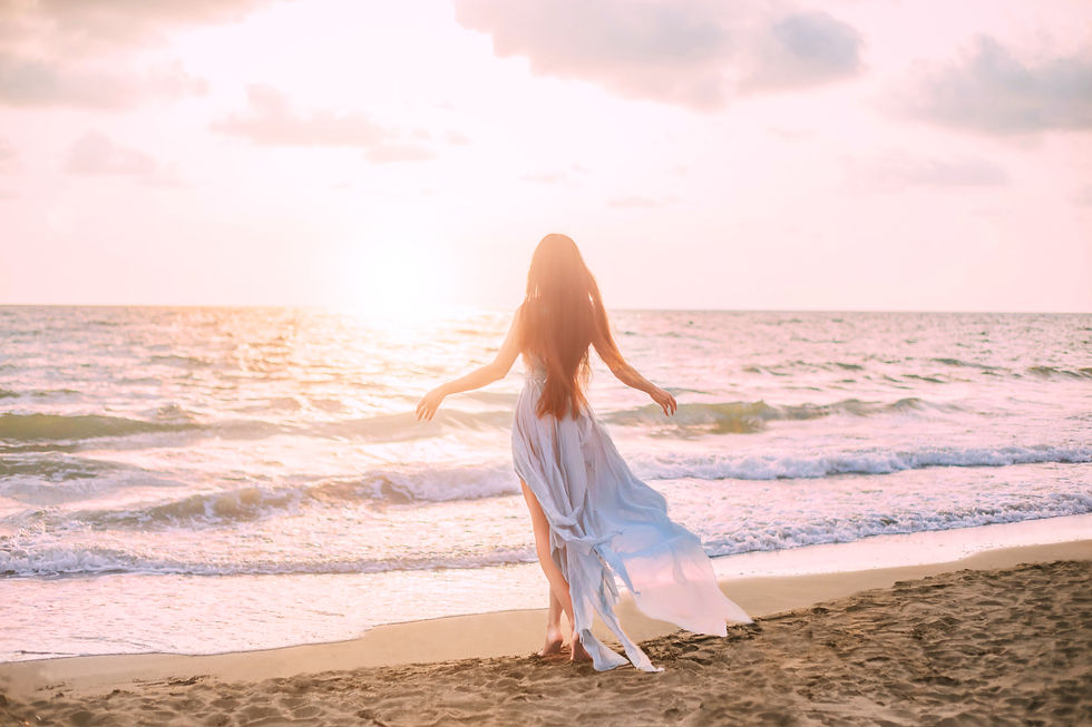 Woman in white standing by the ocean with arms open, symbolizing spiritual renewal, emotional healing, and inner peace