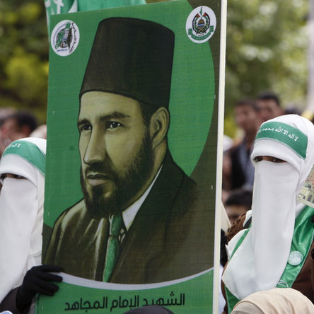 Palestinian women in Gaza display a poster of Muslim Brotherhood founder Hassan al-Banna. Hamas’s ideological lineage is rooted in the Brotherhood, now fading as Saudi Arabia, Egypt, and Qatar move to dismantle its legacy