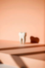 Stylized ceramic tooth sculpture casting a shadow on a peach-toned background at Dental Creations Inc.
