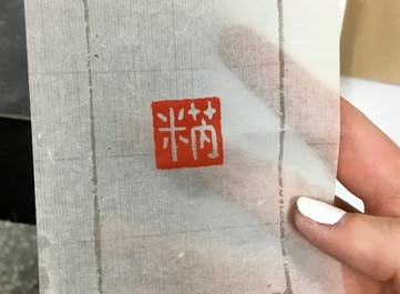 Red Chinese seal stamp impression on thin paper, held up to light.