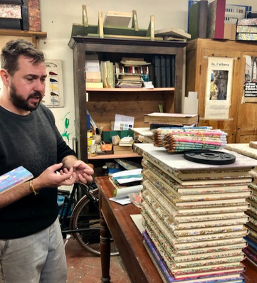 Artisan explaining paper marbling and bookbinding techniques inside Legatoria Firenze workshop surrounded by handmade papers.