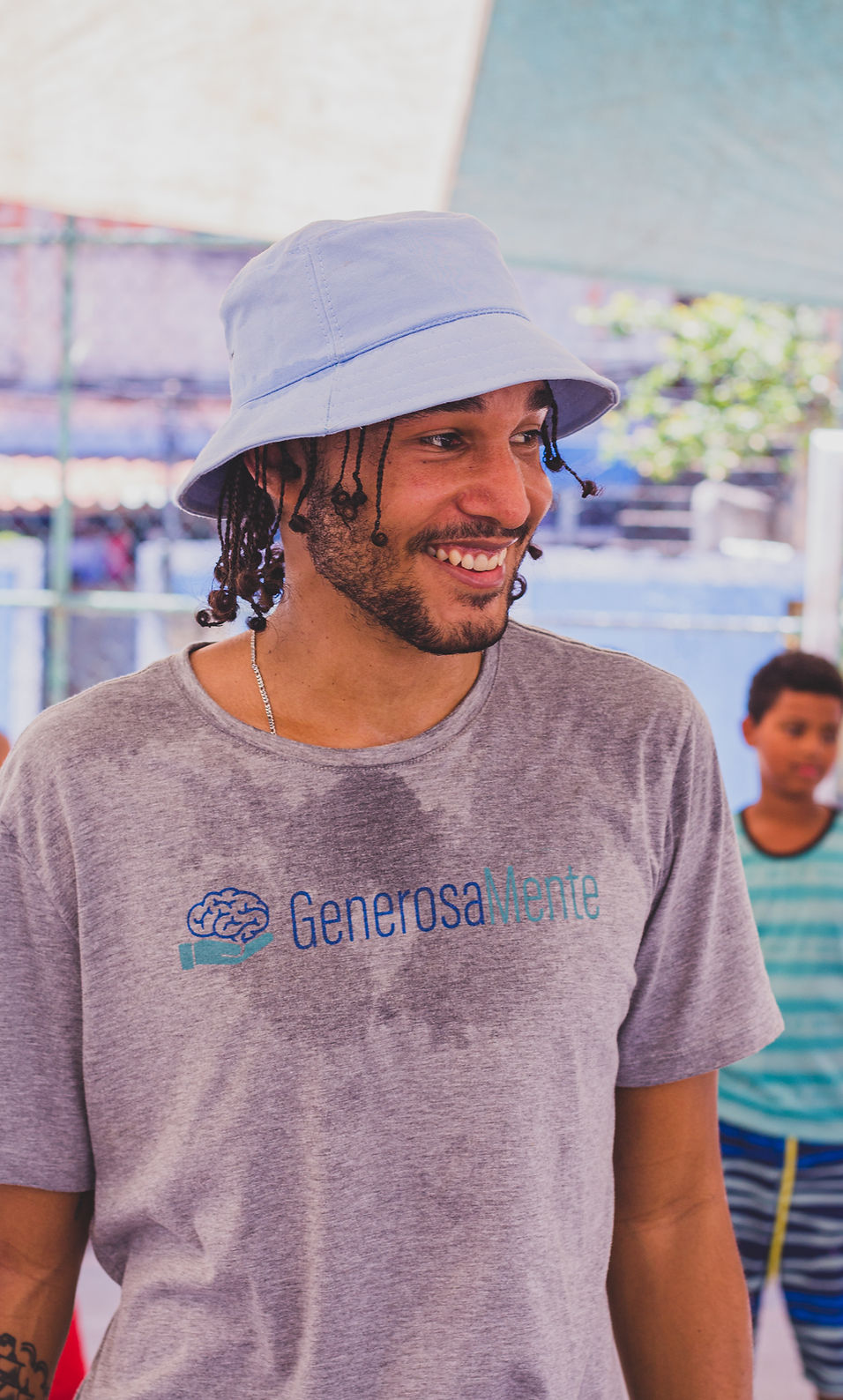 Voluntário de pele negra e cabelo e barba castanhas escuras usando camisa do projeto sorrindo