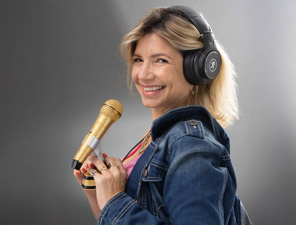 אישה מחייכת מחזיקה מיקרופון זהוב, לובשת אוזניות, ברקע אפור, קורס פודקאסט.