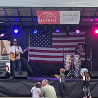 Man playing guitar on stage, American flag backdrop. Audience watches and applauds.