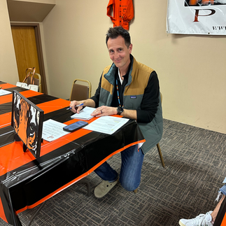 Man smiles at a table, Plenty Wood logo banner, with pen, paper, and PEAF