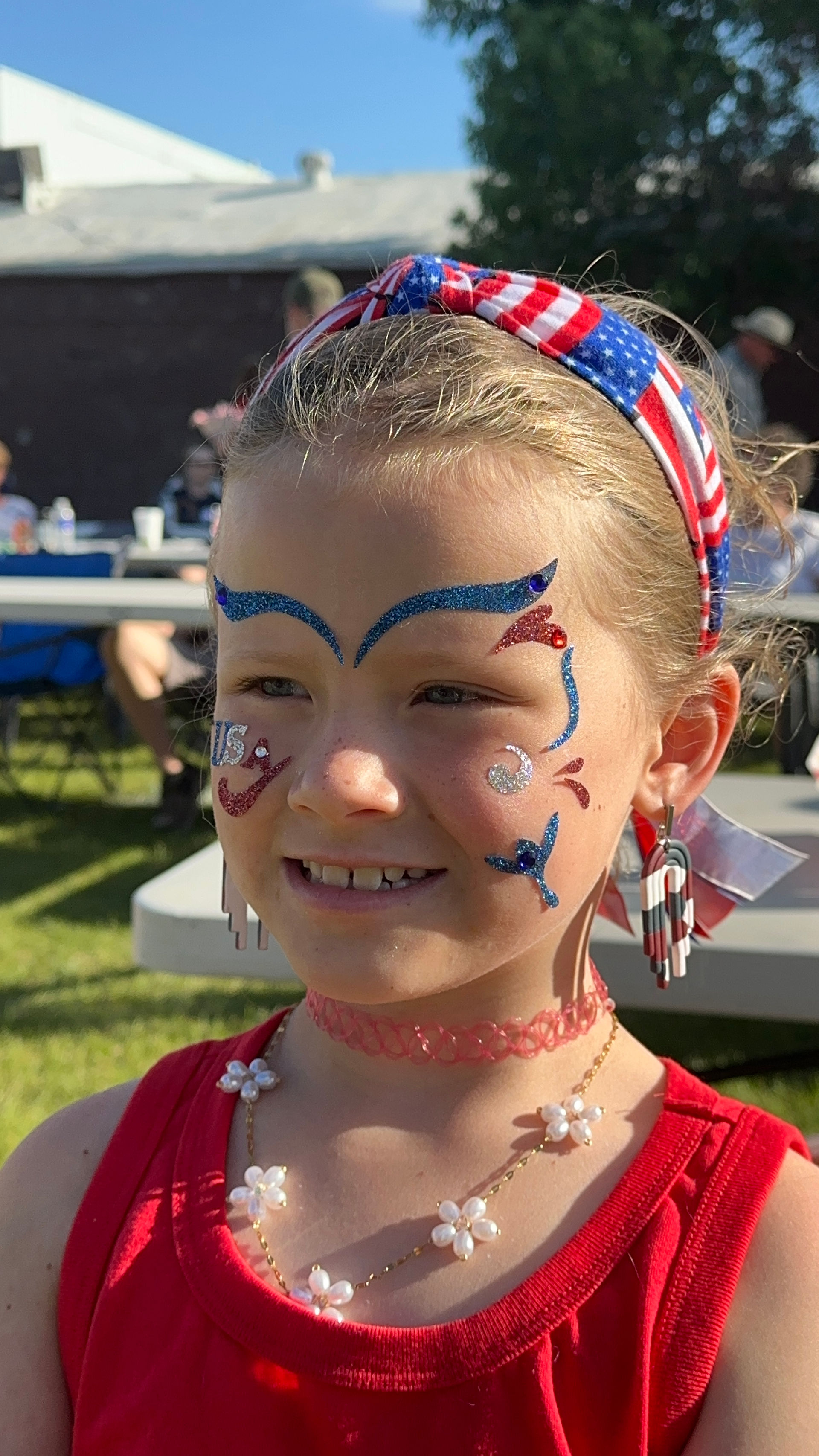 Smiling girl with patriotic face paint, red shirt, and headband at an event