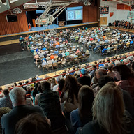 Large crowd in a gymnasium, all-school reunion, watching a presentation, seated.