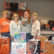 Four women stand proudly with merchandise display, ready for sale.
