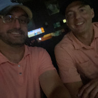 Two men wearing pink shirts smiling at night in dimly lit room.