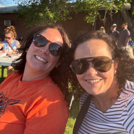 Two smiling women wearing sunglasses posing outdoors with All-School Reunion.