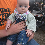 Baby in floral bib held by person, looking curiously at the camera, PEAF