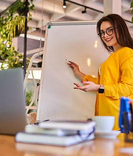 Une jeune femme avec un pull jaune écrit sur un tableau balnc