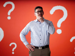 A man standing up holding his hand at his chin thinking. - Paula Donnan Advisory