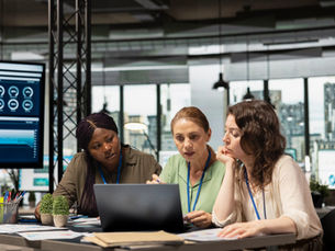 Three prpfessional women discussing a work projects around a laptop.