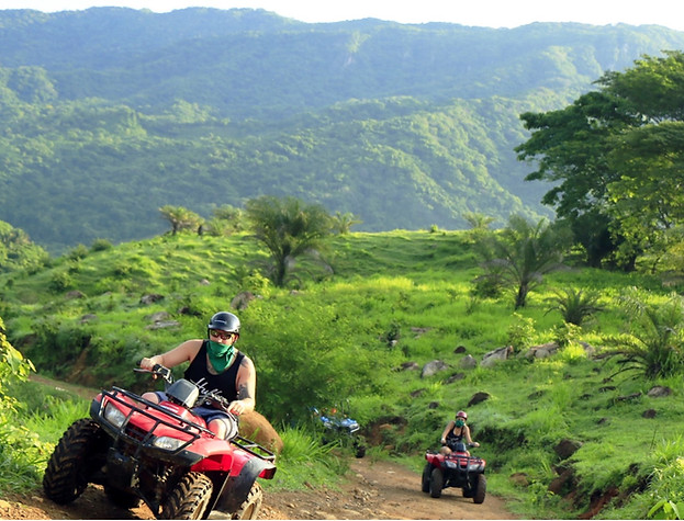 A man on an ATV with beautiful green mountains behind him