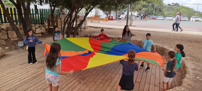 ילדים משחקים במשחק בד רב צבעוני בחצר בית ספר