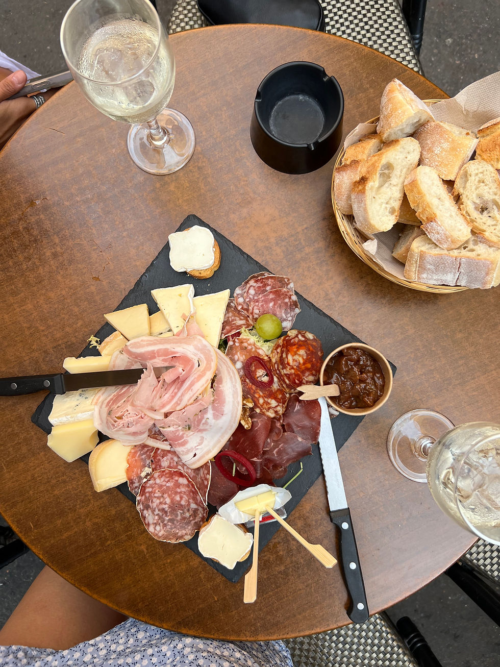 A charcuterie board on top of a brown table with two glasses of white wine. Setting is in Aix-en-Provence.