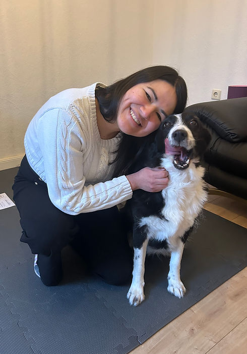 Hundephysiotherapeutin lehnt sich zu ihrem schwarz‑weißen Hund; ruhige Szene im Innenraum mit Nähe.