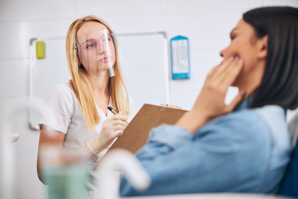 Female patient explaining dental pain to female dental assistant