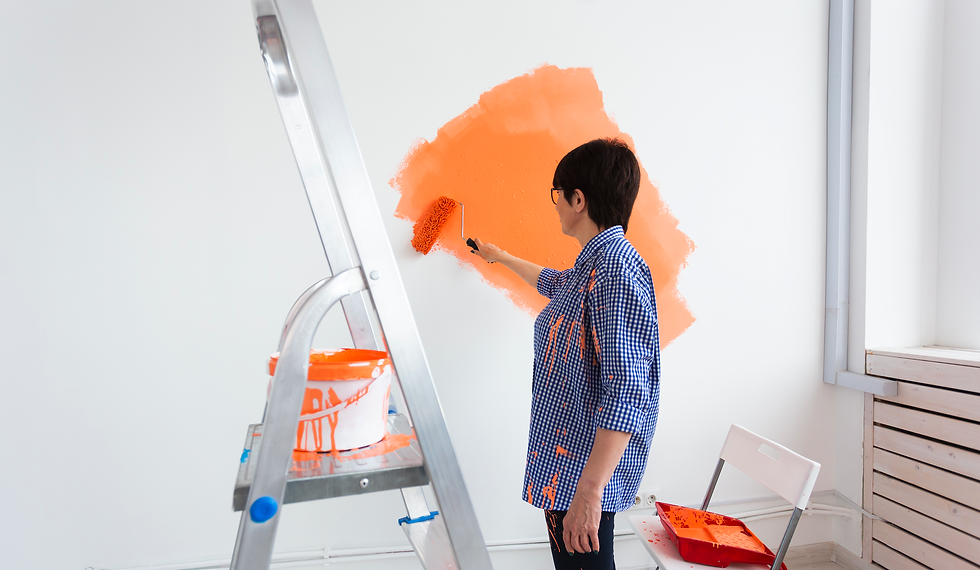 Woman in a blue shirt painting a room with orange paint, paint splashes are on her shirt