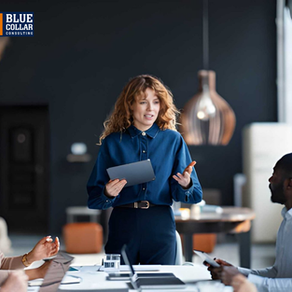 A woman in blue talks to colleagues in an office, holding a tablet. Black background, modern decor. "Blue Collar Consulting" logo visible.