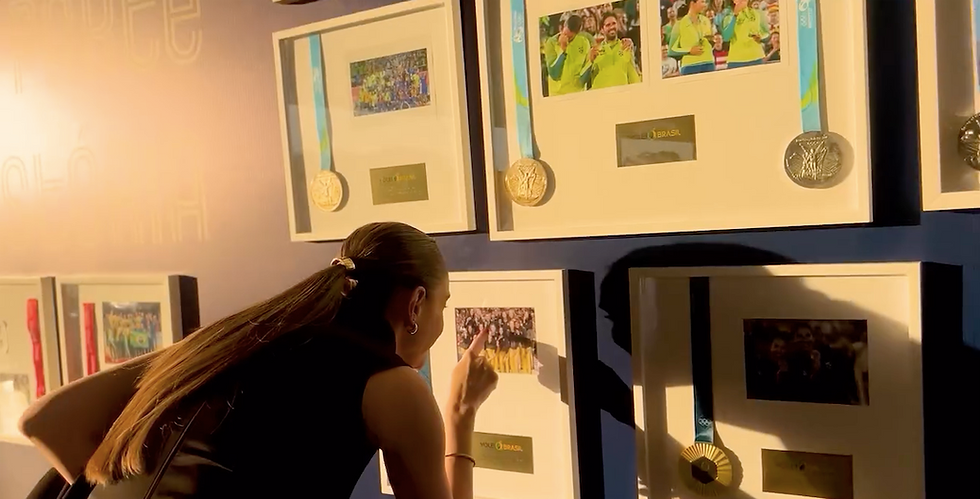 Mulher aponta para foto em molduras com medalhas, em parede azul de exposição, clima de admiração.